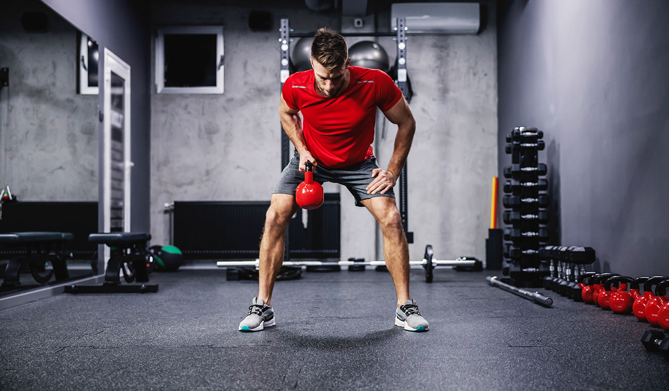 Athletic Male doing Kettle Ball Snatches in a red t-shirt