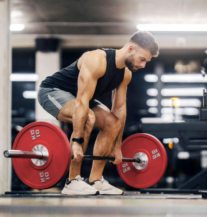 muscular guy in black tank top and grey shorts doing 10kg deadlift