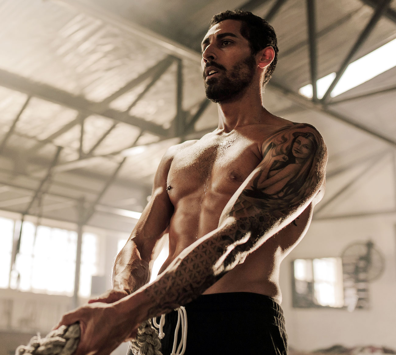 Muscular guy with tattoo on left arm holding a rope