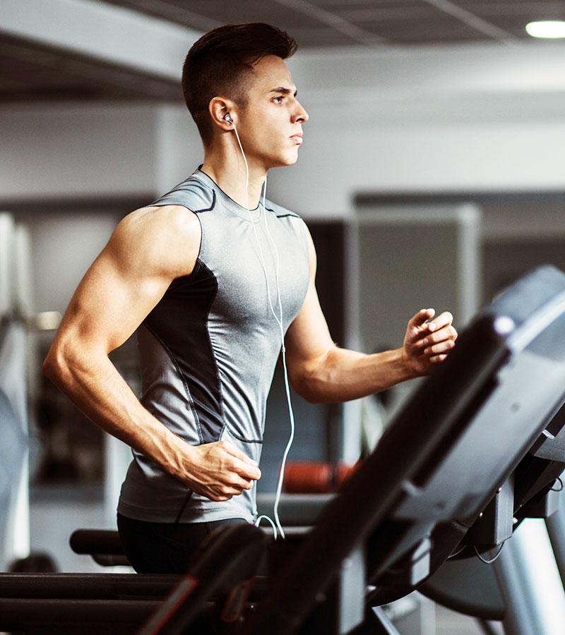 athletic male listening to music running on a treadmill in a grey tank top