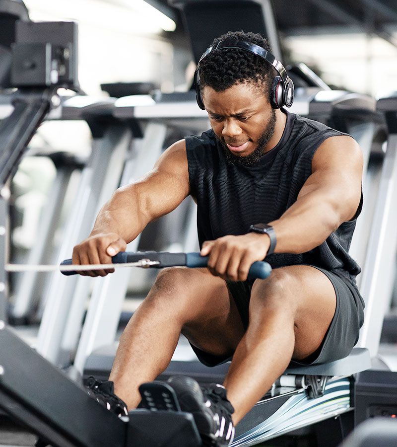 muscular guy using the cable rower listening to music