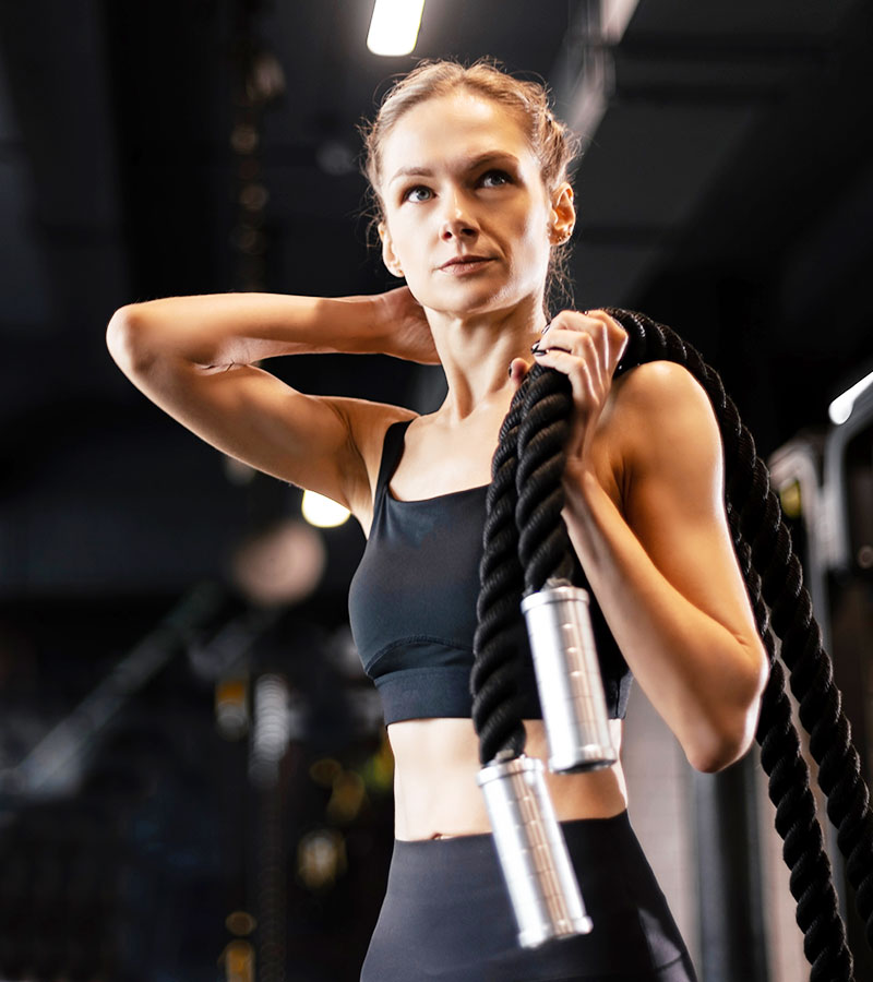 athletic girl holding ropes on her shoulders in a black sports bra